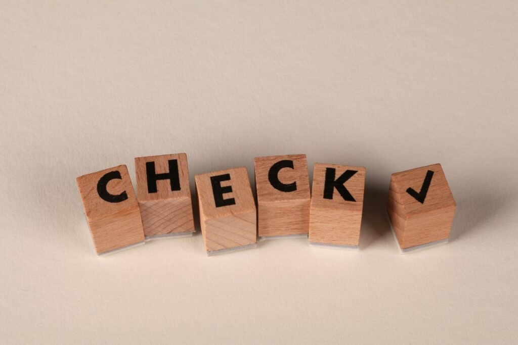 Wooden blocks aligned to spell 'CHECK' with a checkmark symbol on a neutral background.