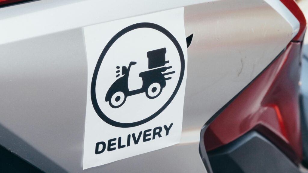 A delivery sticker featuring a scooter on a motorcycle's metallic surface.